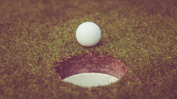 컵의 입술에 골프 공입니다. 골프 코스의 푸른 잔디에서 골프 볼 — 스톡 사진