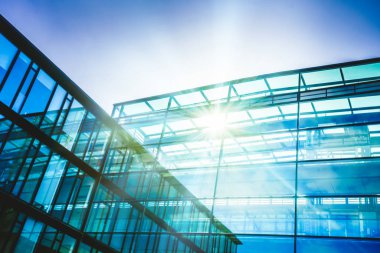 Mavi gökyüzünde güneş ışınları ile gökdelen cam cepheler. Modern