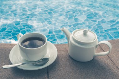 Fincan havuzun yanındaki masada. Beyaz seramik kahve fincanı 