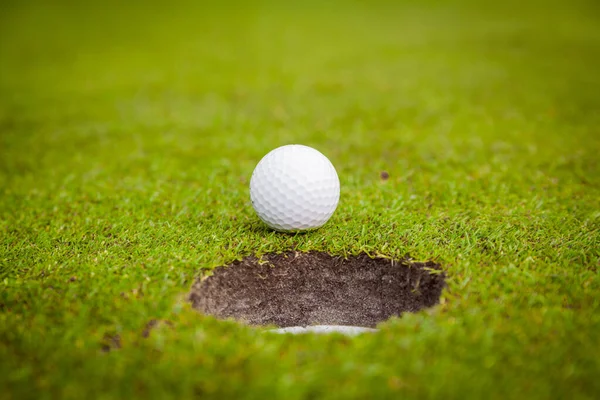 Golf ball on green meadow. golf ball on lip of cup — Stock Photo, Image