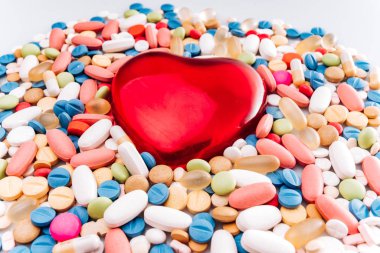 Çeşitli ilaç hapları, tablet ve kalp şeklinde bir biblo. Hapların arka planı. Çeşitli ilaç tabletleri ve haplar beyaz arka planda farklı renklerde. Sağlık