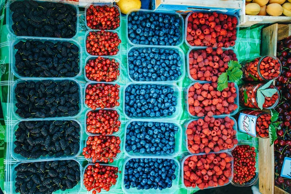 Uma mistura de bagas frescas no mercado, morangos, mirtilos, framboesas, amoras, cerejas e groselhas vermelhas — Fotografia de Stock