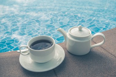 Fincan havuzun yanındaki masada. Beyaz seramik kahve fincanı 