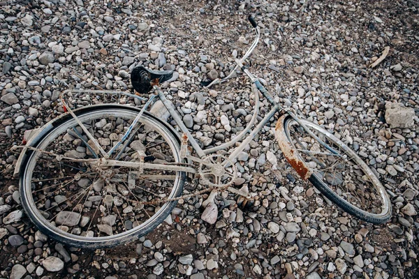 Uma velha bicicleta abandonada numa praia de telhas. Bicicleta velha com ferrugem . — Fotografia de Stock