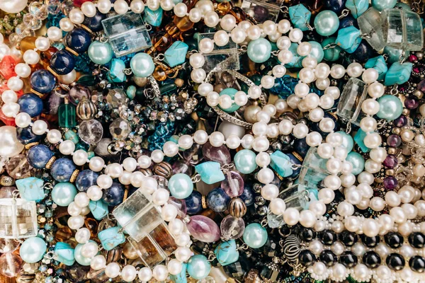 Beads and necklaces made of colored semi precious stones. Background from a variety of beautiful jewelry, multi-colored turquoise stones, amber, cat's eye, pearls. — Stock Photo, Image