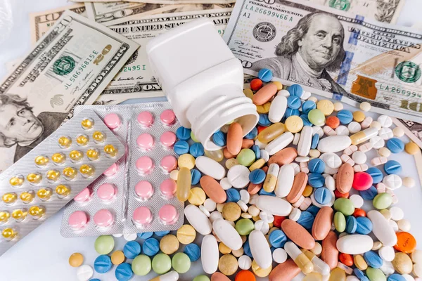 Множество медицинских таблеток разных цветов и капсул на долларовых купюрах, вид сверху — стоковое фото