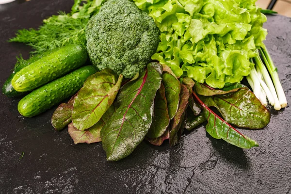 Un mélange de produits frais sur une table noire. Aneth, poivron vert, persil, concombres, brocoli, oignons, feuilles de borax . — Photo