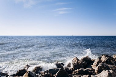 Beyaz bir ibikli dalga siyah lav kayalarına çarpar.