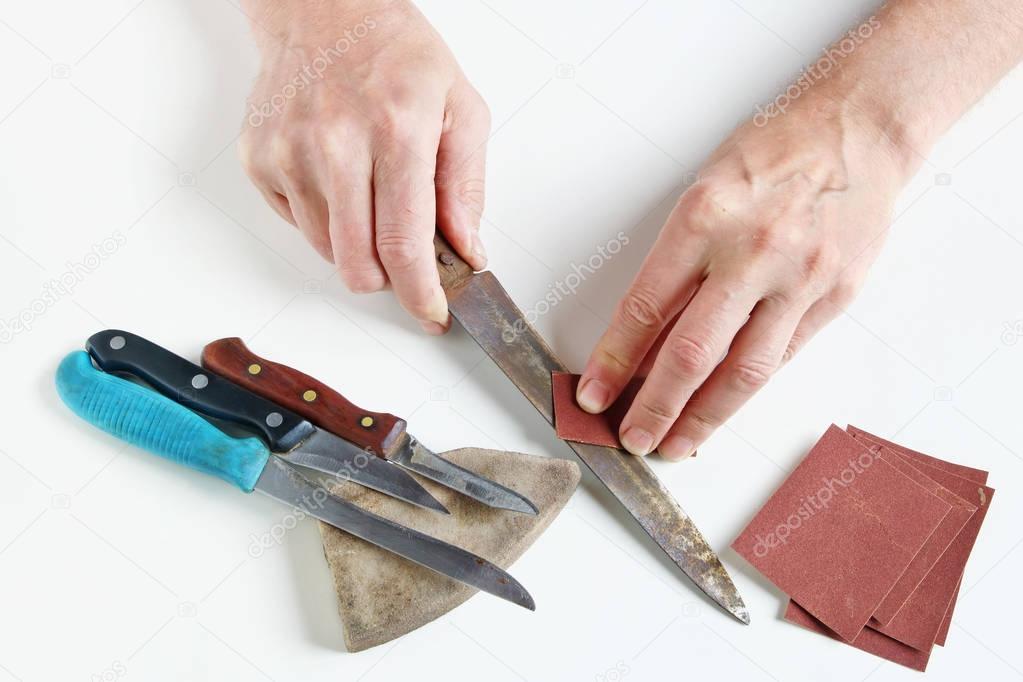 Old master tries to sharpen rusty kitchen knives on his white de