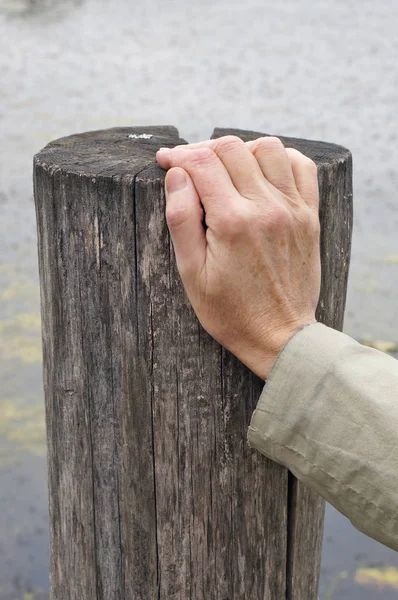 The elderly grandmother rests his right hand on a wooden pillar — Stock Photo, Image