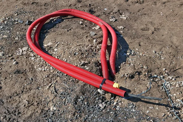 On clay soil lies a power cable in red plastic protective armor — Stock Photo, Image