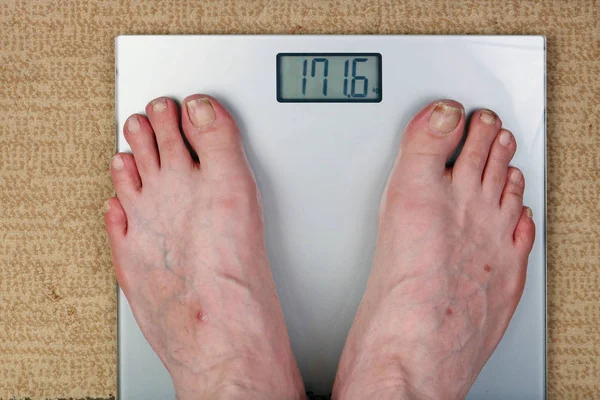 Yaşlı bir adam elektrik terazisinde ağırlığını kontrol eder.