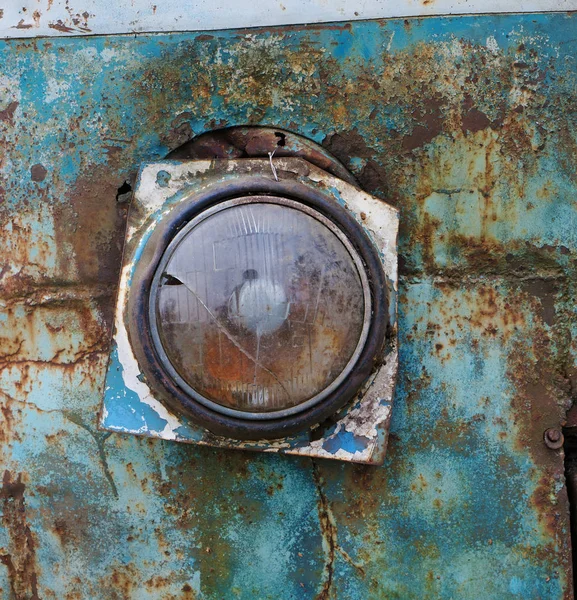 Broken glass headlight on the rusty iron of a blue rotten bus