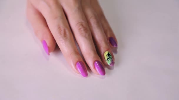 Female hand with colorful manicure work, purple nail polish, palm tree picture