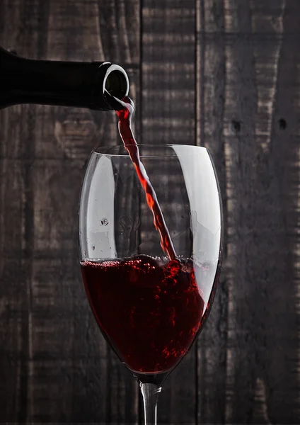 Gieten van rode wijn in het glas uit fles — Stockfoto