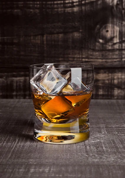 Glasss of whiskey with ice cubes on wood — Stock fotografie
