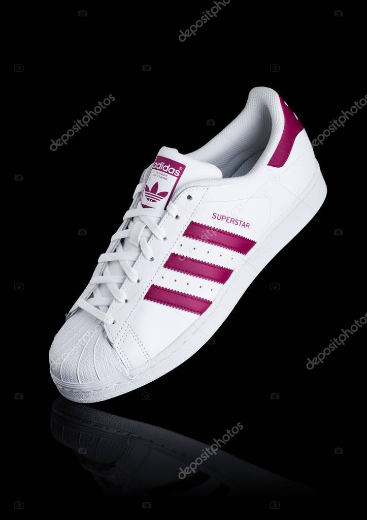 LONDON, UK - JANUARY 12, 2018: Adidas Originals Superstar red shoes on black background.German multinational corporation that designs and manufactures sports shoes, clothing and accessories.