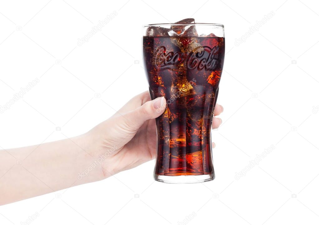 LONDON, UK - JANUARY 20, 2018: Female hand holds glass of Coca Cola drink on white background. The drink is produced and manufactured by The Coca-Cola Company.