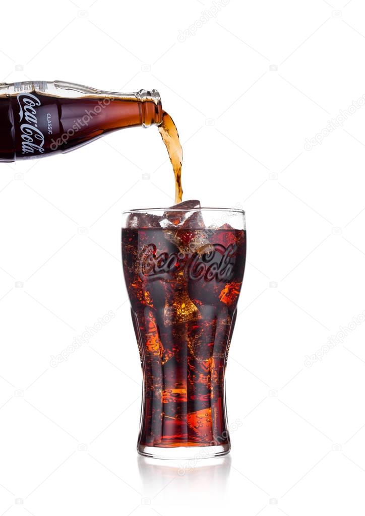 LONDON, UK - JANUARY 20, 2018: Pouring Coca Cola soda drink from bottle to glass on white background. The drink is produced and manufactured by The Coca-Cola Company.