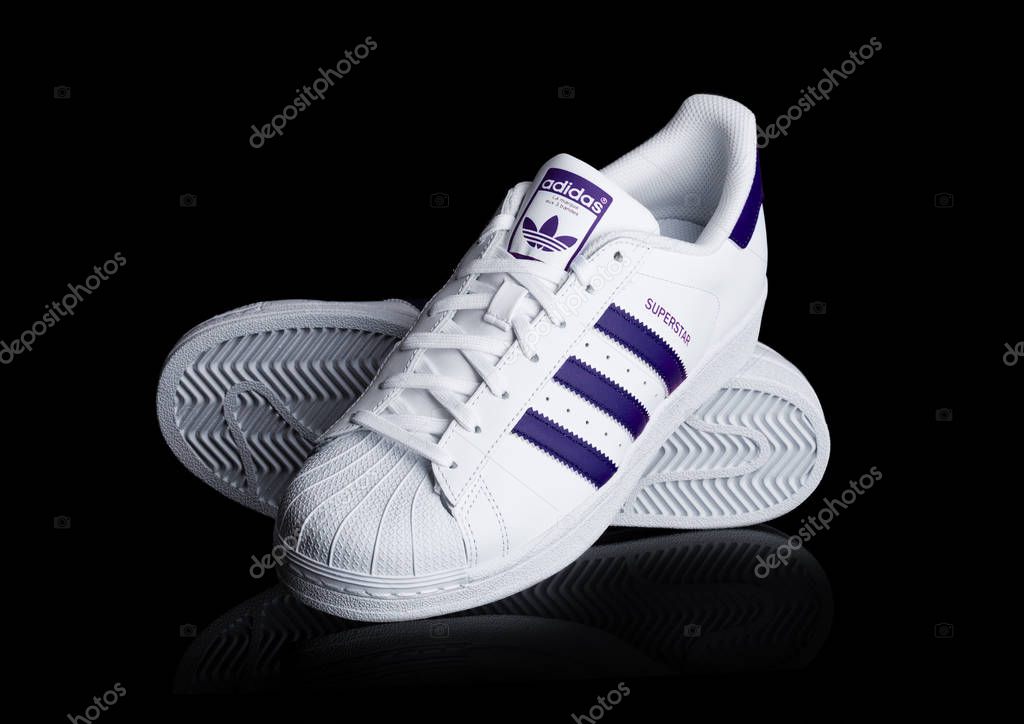 LONDON, UK - JANUARY 24, 2018: Adidas Originals Superstar blue shoes on black background.German multinational corporation that designs and manufactures sports shoes, clothing and accessories.