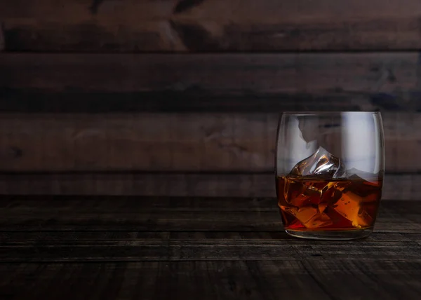 Glass of whiskey with ice cubes on wooden table — Stock Photo, Image
