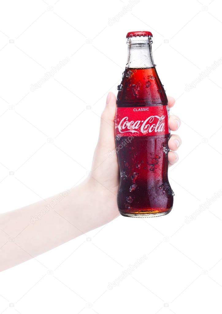 LONDON, UK - FEBRUARY 14, 2018:  Female hand holds glass bottle of Classic Coca Cola on white background. The drink is produced and manufactured by The Coca-Cola Company.