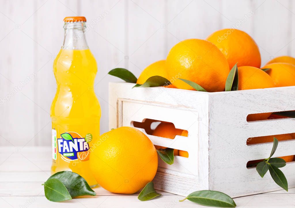 LONDON, UK - MARCH 31, 2018: Glass bottle of Fanta orange soft drink on white wooden background with box of raw oranges