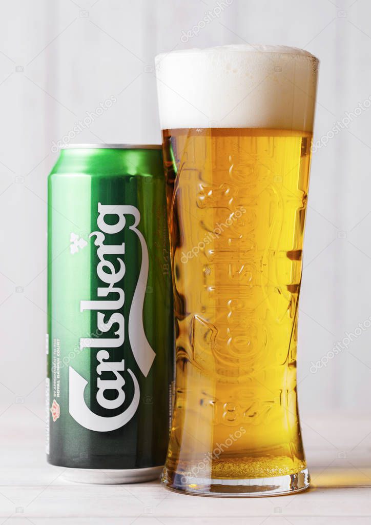 LONDON, UK - APRIL 27, 2018: Cold glass and aluminium can ff Carlsberg beer on wooden background. Danish brewing company founded in 1847.
