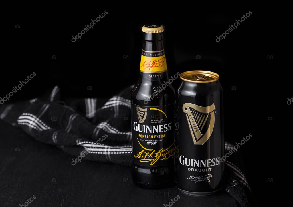 LONDON, UK - APRIL 27, 2018: Bottle and aluminium cans of Guinness draught stout beer bottle on darkwooden background. Guinness beer has been produced since 1759 in Dublin, Ireland.