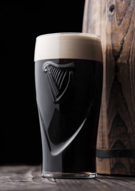 Londra, İngiltere - 03 Mayıs 2018: Orijinal bardak Guinness fıçı şişman bira koyu ahşap arka plan üzerinde ahşap varil yanındaki.
