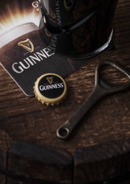 Londra, İngiltere - 03 Mayıs 2018: Orijinal bardak Guinness fıçı şişman bira şişe açacağı ve bira altlığı ile ahşap varil üzerine.