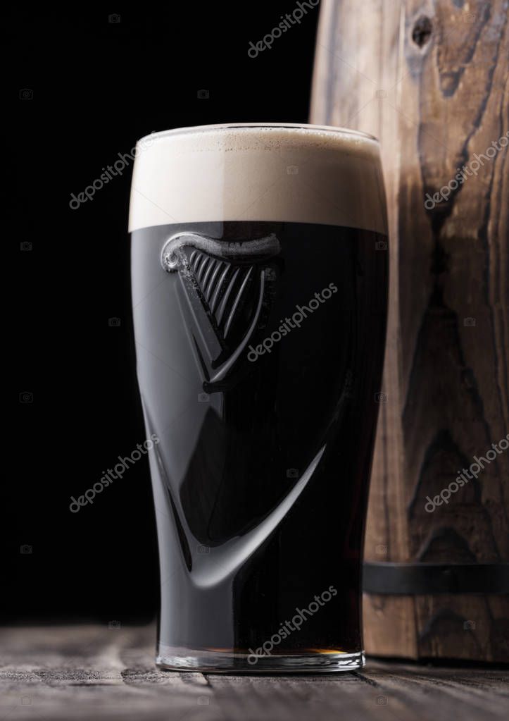 LONDON, UK - MAY 03, 2018: Original glass of Guinness draught stout beer next to wooden barrel on dark wooden background.Guinness beer has been produced since 1759 in Dublin.