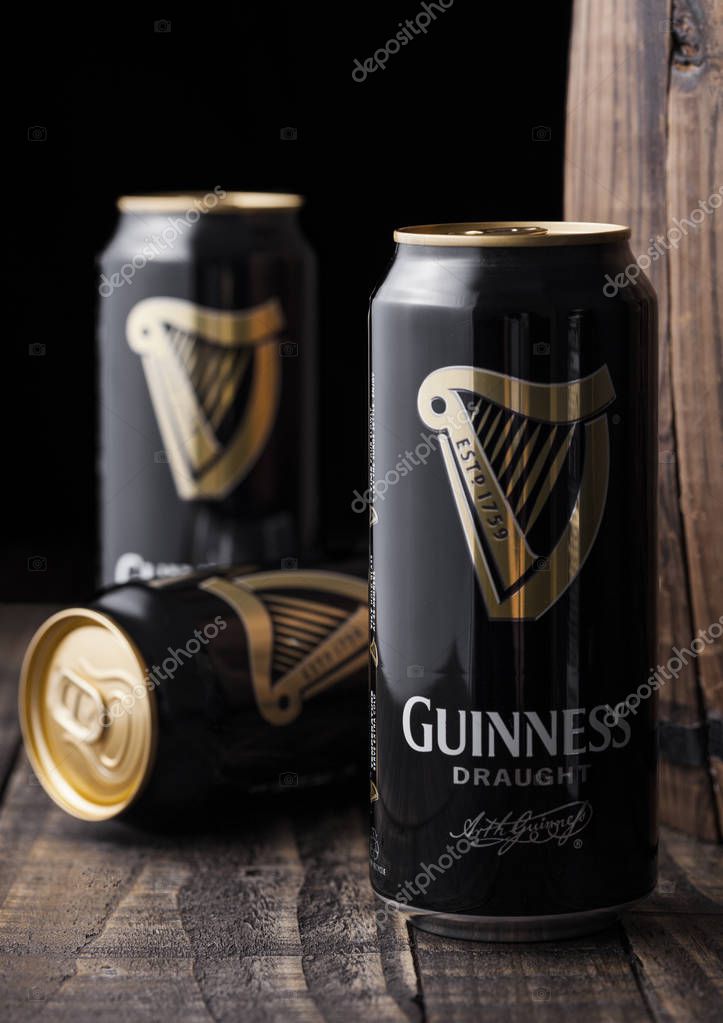 LONDON, UK - MAY 03, 2018: Aluminium cans of Guinness draught stout beer next to wooden barrel on dark wooden background. Guinness beer has been produced since 1759 in Dublin, Ireland.