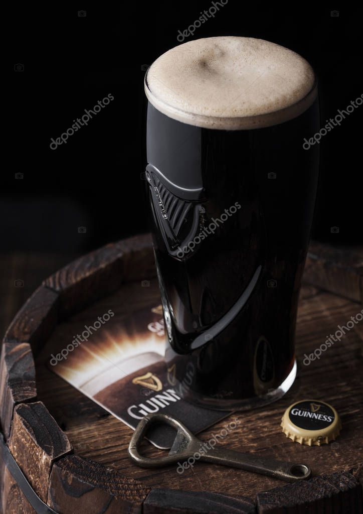 LONDON, UK - MAY 03, 2018: Original glass of Guinness draught stout beer on top of  wooden barrel with bottle opener.Guinness beer has been produced since 1759 in Dublin.