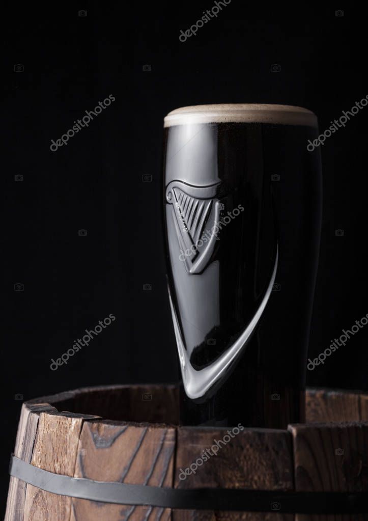 LONDON, UK - MAY 03, 2018: Original glass of Guinness draught stout beer on top of  wooden barrel on dark wooden background.Guinness beer has been produced since 1759 in Dublin.