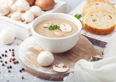 Beyaz tabak kremalı kestane mantarı çorbası beyaz mutfak arka planında ve bir kutu çiğ mantar ve taze ekmek..