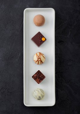 Lüks çikolatalı şekerlemeler siyah masa arkaplanındaki beyaz porselen tabakta. Beyaz, siyah ve sütlü çikolata çeşitleri..