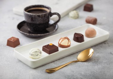 Lüks çikolatalı şekerler beyaz porselen tabakta, bir fincan sade kahve ve arka planda altın kaşık..