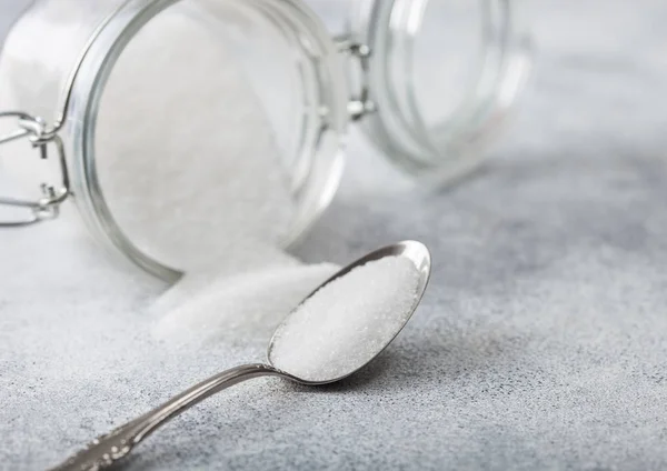 Glass jar of natural white refined sugar with silver spoon on light table background. — Stock Photo, Image