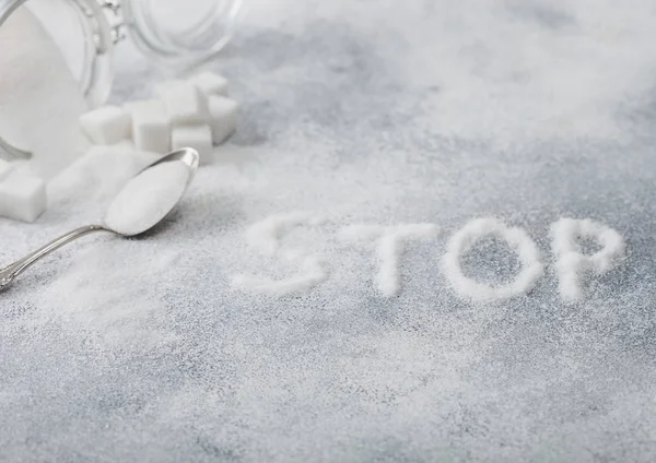 Skleněná sklenice přírodního bílého rafinovaného cukru s kostkami se stříbrnou lžičkou na pozadí světlého stolu s písmeny Stop. Koncept nezdravých potravin. — Stock fotografie