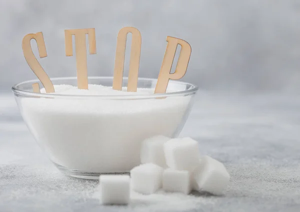 Szklana miska naturalnego białego cukru rafinowanego z kostkami na jasnym tle stołu z literami Stop. Niezdrowa koncepcja żywności. — Zdjęcie stockowe
