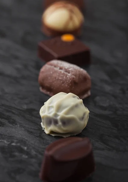 Selección de caramelos de chocolate de lujo en tablero de marbel negro. Surtido de chocolate blanco, oscuro y de leche . — Foto de Stock