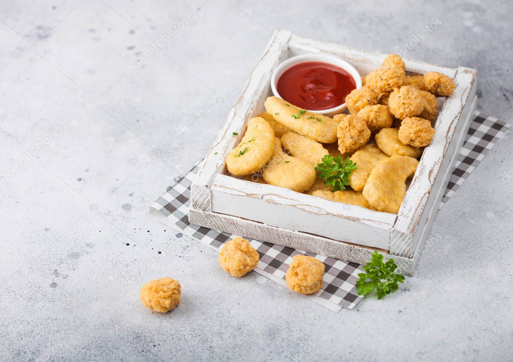Buttered chicken nuggets and popcorn bites in white vintage wooden box with ketchup on light background. 
