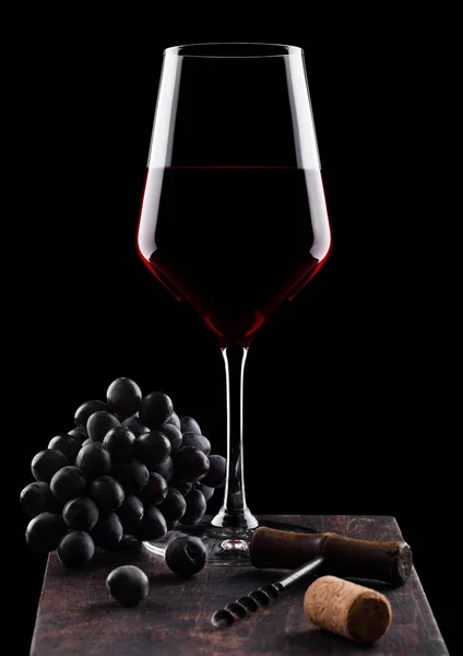 Glas rode wijn met donkere druiven en vintage kurkentrekker opener en kurk op houten bord op zwarte achtergrond. — Stockfoto