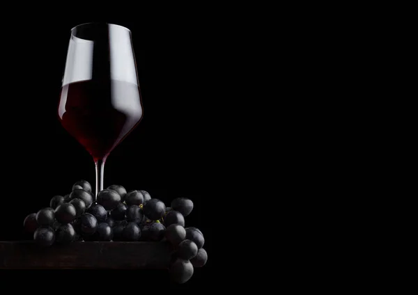 Copo elegante de vinho tinto com uvas escuras em tábua de madeira sobre fundo preto. Espaço para texto — Fotografia de Stock