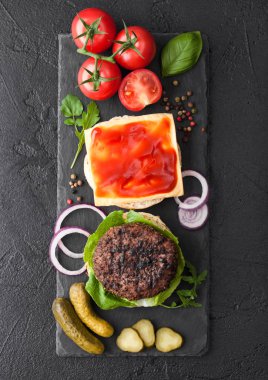 Siyah arka plan üzerinde çörekler soğan ve domates ile taş doğrama tahtası üzerinde Taze ızgara kıyma burger. Tuzlu turşu ve ketçap ile peynir dilimi.