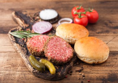 Kaliteli doğranmış hamburgerler, soğanlı çörekler ve ahşap zemin üzerinde domatesler. Metin için boşluk