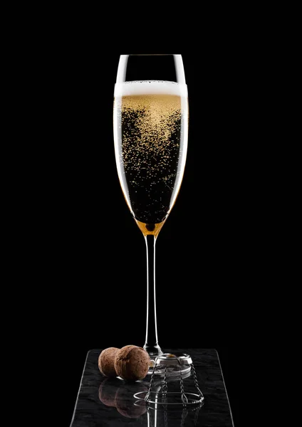 Elegancki kieliszek żółtego szampana z korkową i drucianą klatką na czarnej marmurowej desce na czarnym tle. — Zdjęcie stockowe