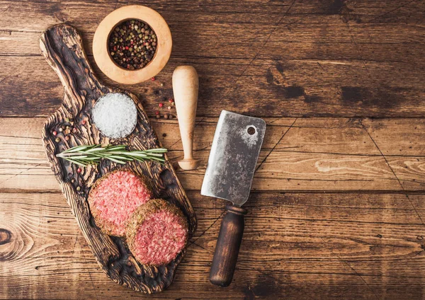 Burgers de bœuf au poivre haché cru frais sur planche à découper vintage avec mortier et pilon et hache de viande sur fond en bois . — Photo