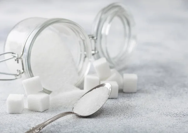 Glass jar of natural white refined sugar with cubes with silver spoon on light table background. — Stock Photo, Image